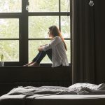 Canva-Lonely-sad-young-woman-sitting-on-windowsill-at-home
